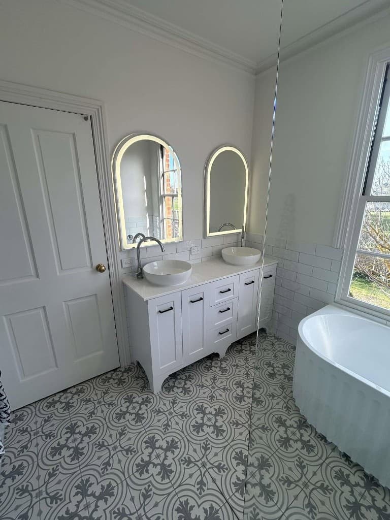 Double vanity with arched backlit mirrors and freestanding bath